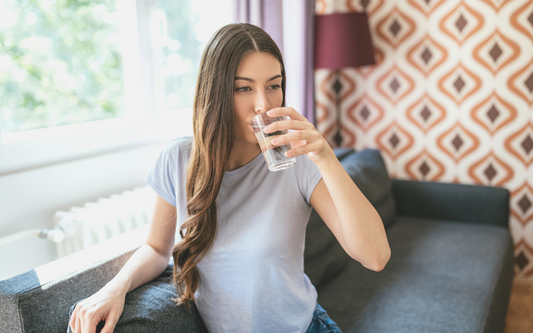 woman sitting on couch taking mushroom supplements with water